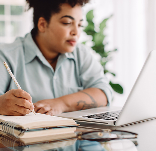 Woman looking at laptop and writing in notebook