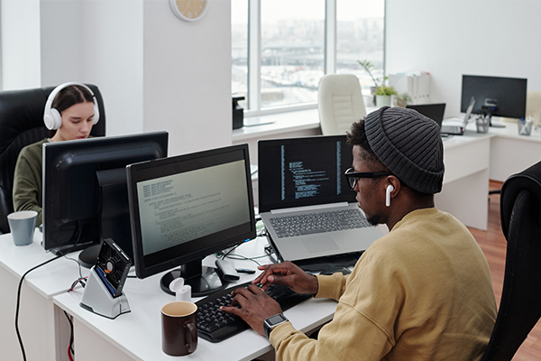 Two people using computers and sitting at a desk